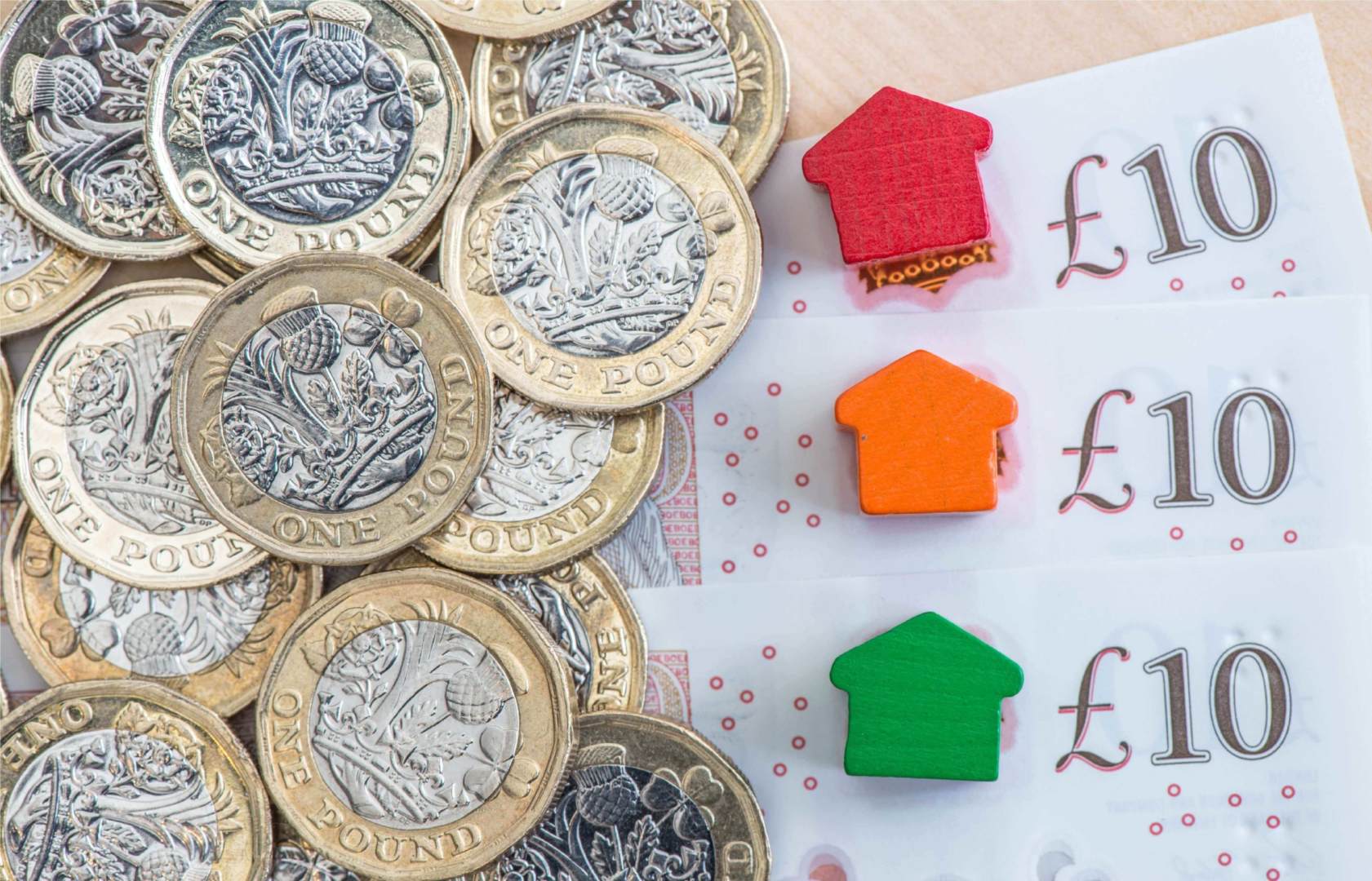 Coins pile on a small stack of £10 notes with multi colour home shaped blocks on top