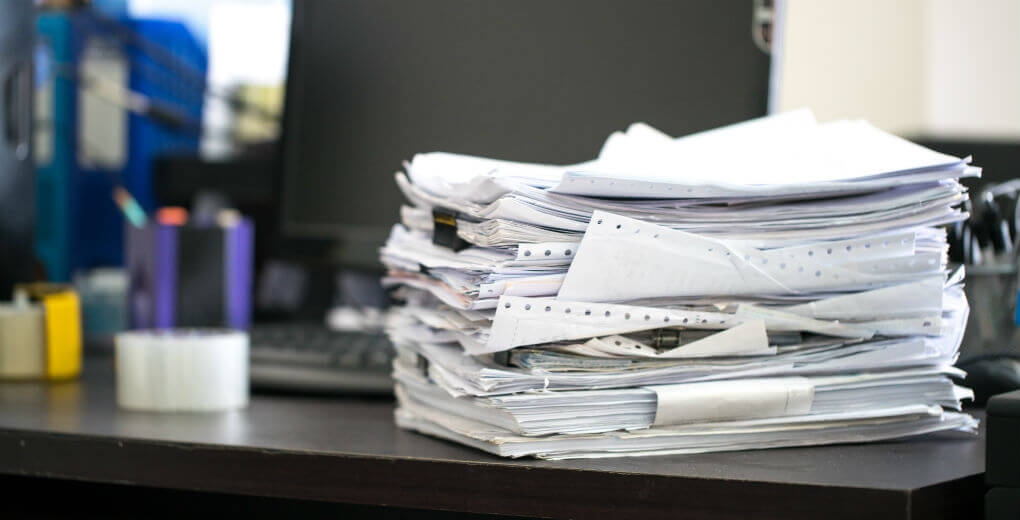 A big stack of paperwork on a work desk